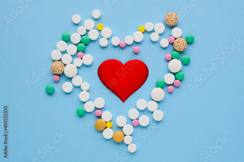 Many different tablets in the shape of heart and red heart on blue background. Medical flat lay . Valentine's Day. World Pharmacist's Day photo