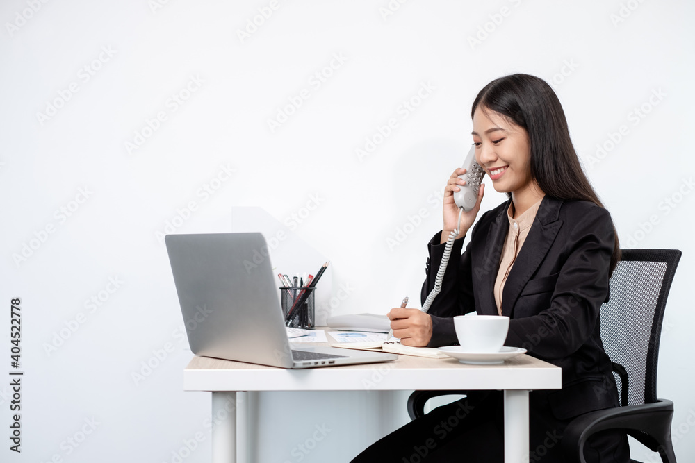 Asian businesswoman talking on the phone and working on a laptop with a cheerful and happy smile while working at the office Asian businesswoman talking on the phone and working on a laptop with a cheerful and happy smile while working at the office