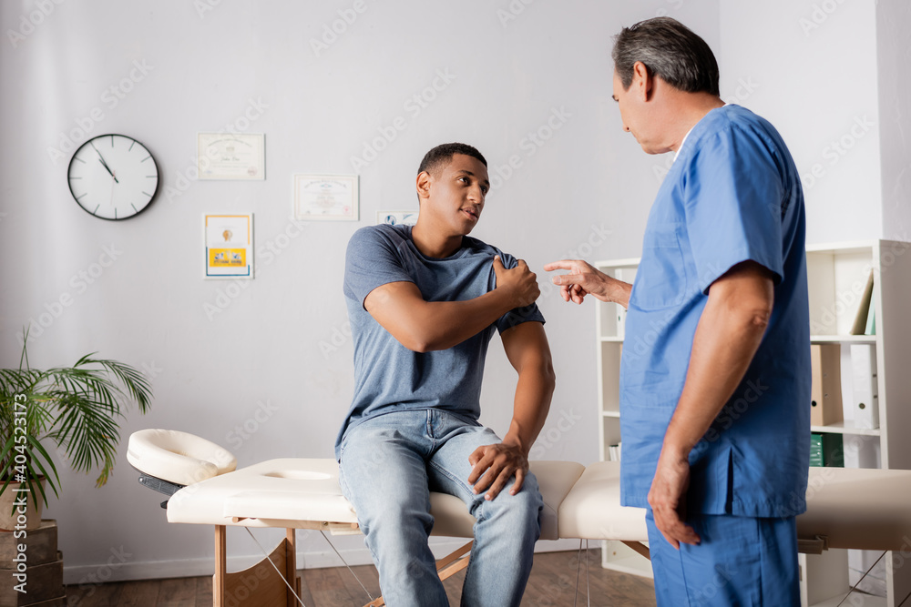 Obraz premium doctor pointing with finger at injured arm of african american patient