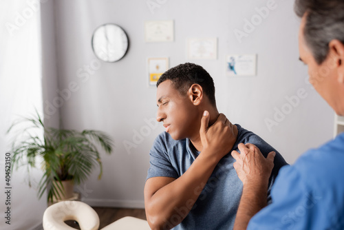 injured african american man touching neck near doctor on blurred foreground
