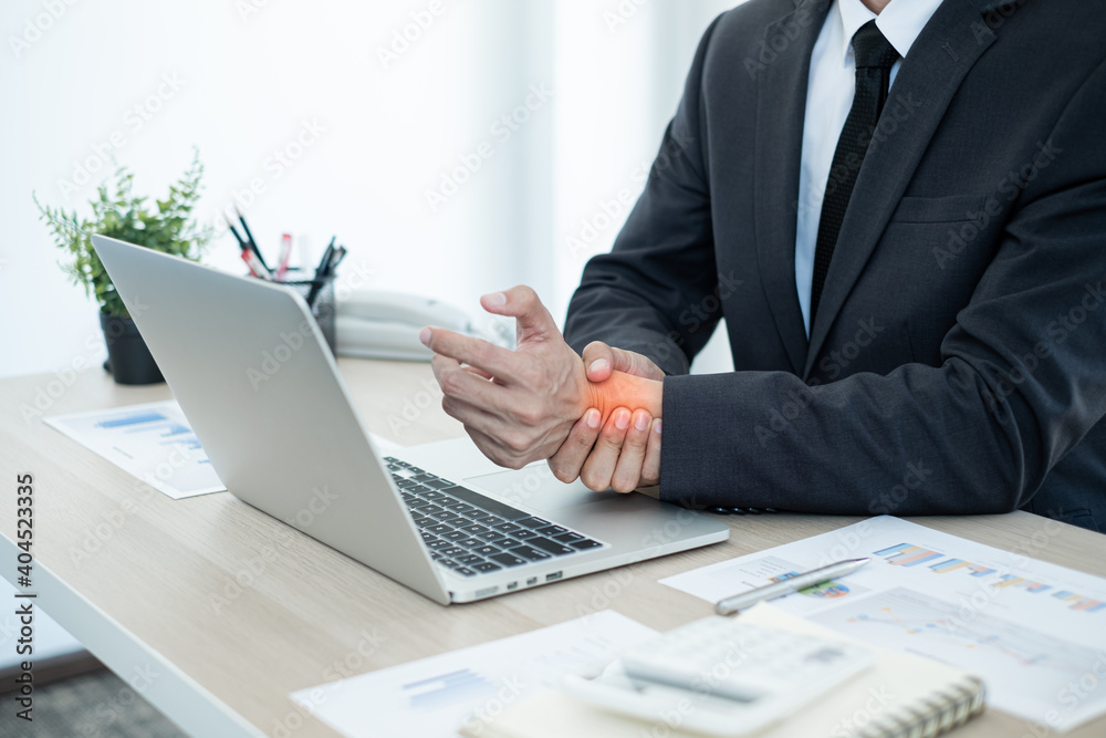 Businessman grasping the painful wrist caused by prolonged work on a laptop keyboard. Wrist numbness Arthritis While working at the office Businessman grasping the painful wrist caused by prolonged work on a laptop keyboard. Wrist numbness Arthritis While working at the office
