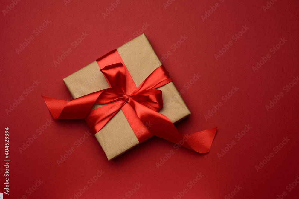square gift box is packed in red paper and curled silk ribbon on a red background, festive background square gift box is packed in red paper and curled silk ribbon on a red background, festive background
