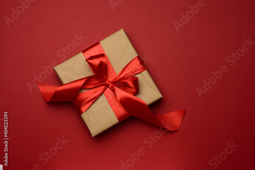 square gift box is packed in red paper and curled silk ribbon on a red background, festive background