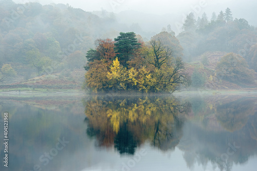 Misty autumn morning by Rydal Water with stunning fall colours and reflection