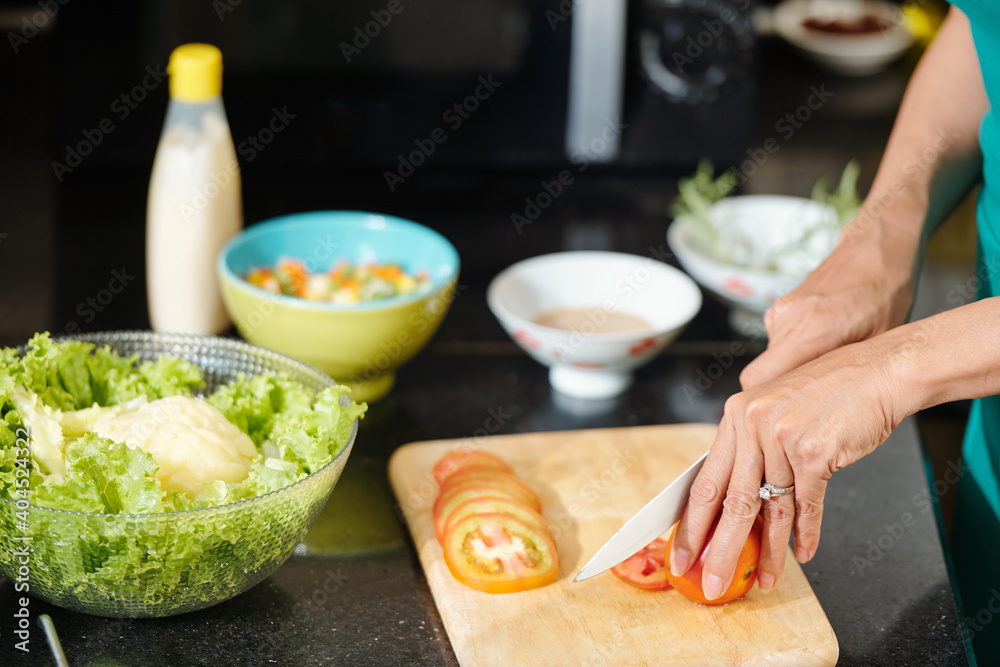 Close-up image of housewife cutting fresh tomatoes with sharp knofe when making salad at kitchen counter Close-up image of housewife cutting fresh tomatoes with sharp knofe when making salad at kitchen counter