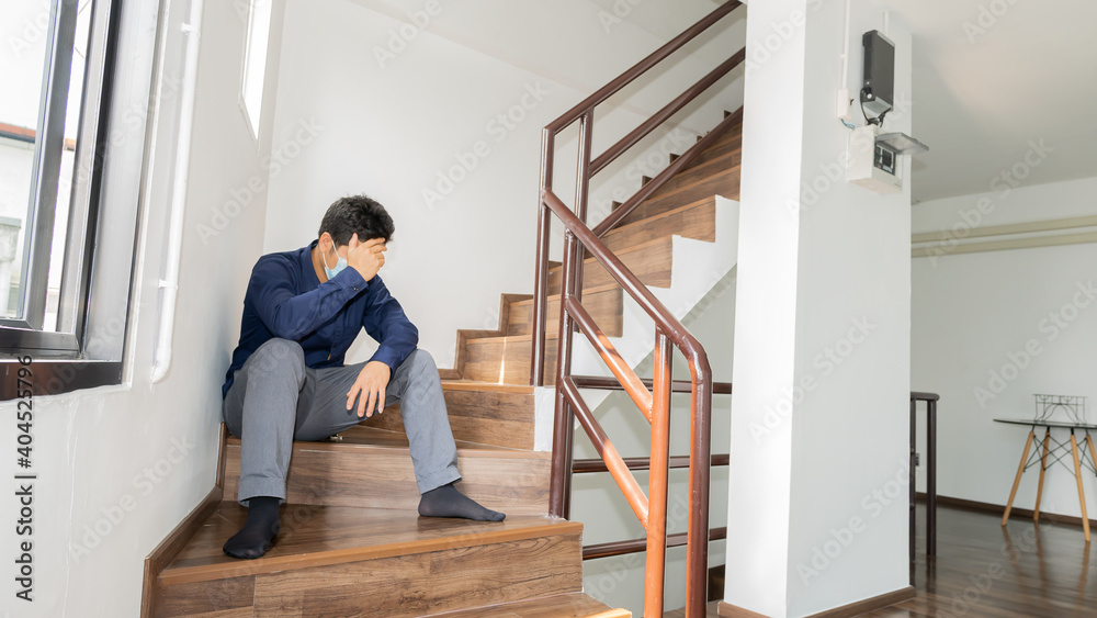 A young man in a blue shirt was stressed and sat sad from losing his job on the stairs of the building.