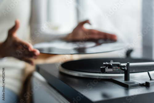 partial view of african american woman holding vinyl disc near record player, blurred background