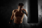 Aggressive boxer training defense and attacks in boxing bag on black background with smoke