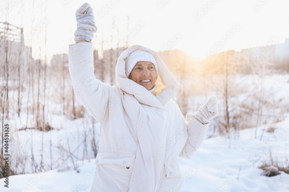 Obraz premium Happy elderly senior mature woman in white warm outwear playing with snow in sunny winter outdoors. Retired healthy people holiday vacation winter activities, active lifestyle concept.