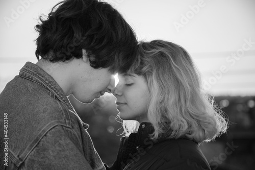 black and white close-up portrait of young couple in love, guy and a teenage girl, against the backdrop of the setting sun. long-awaited meeting, enjoying the moment, tender feelings. Valentine's Day