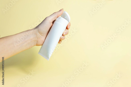 female hand opens white cosmetic tube on a beige background. Hand cream, lotion concept. Winter skin care