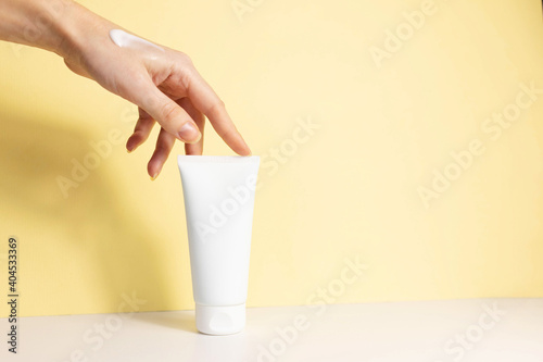 female hand with applied cream touches cosmetic tube on beige background. Concept of cream, hand lotion. Winter skin care photo