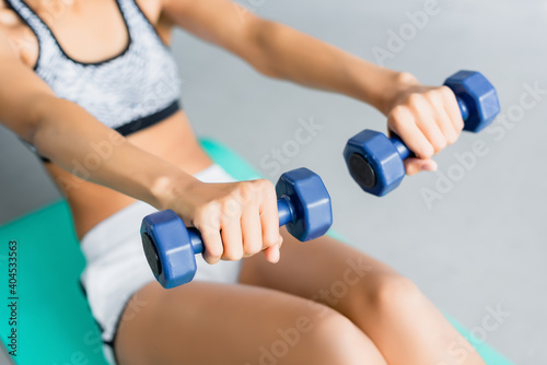 cropped view of african american sportswoman doing abs exercise with dumbbells, blurred background