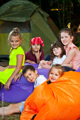 Children rest on a hike. Boys and girls play on an inflatable sofa. Summer vacation in nature. Tents in the background. Games in a tent camp.