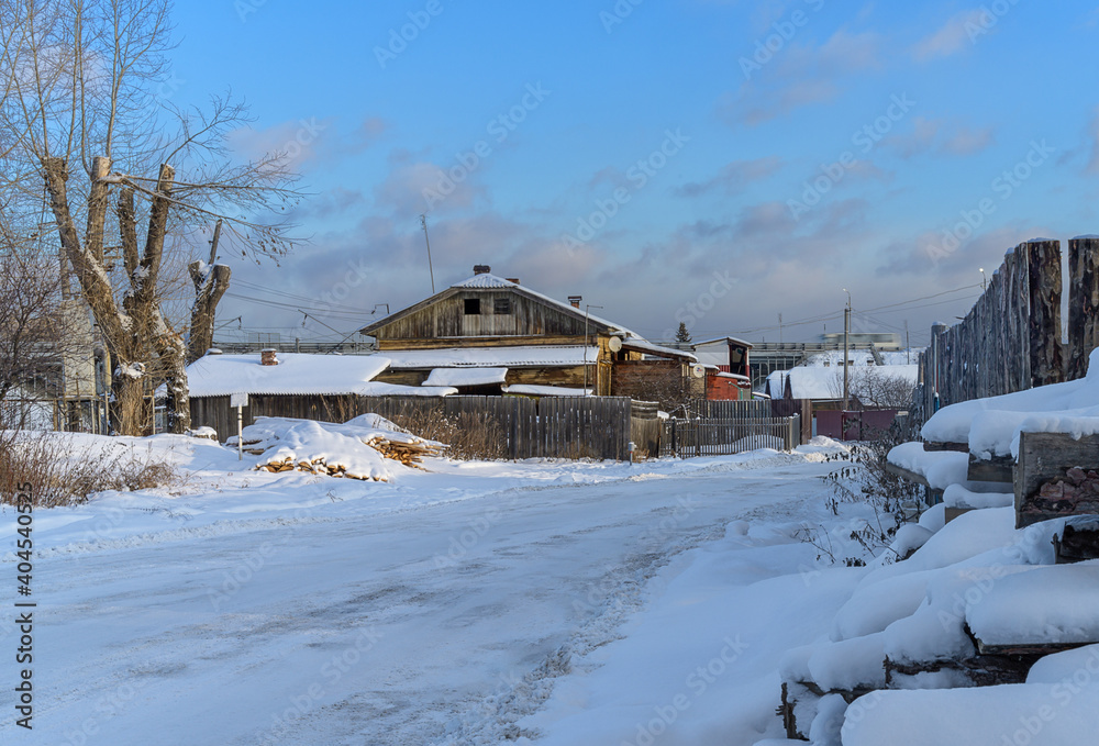 winter in the village. old house in traditional Russian style with firewood and a wooden fence. a lot of white pure snow around. blue sky with white clouds on a clear winter sunny day