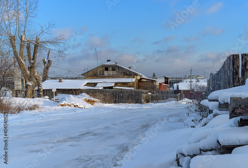 winter in the village. old house in traditional Russian style with firewood and a wooden fence. a lot of white pure snow around. blue sky with white clouds on a clear winter sunny day
