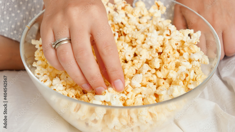 CLoseup of female hand taking popcorn from big glass while watching movie at home CLoseup of female hand taking popcorn from big glass while watching movie at home