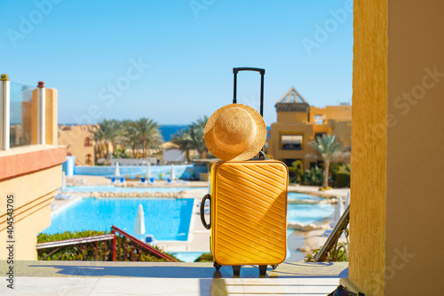 Travel, summer holidays and vacation concept yellow suitcase with hat on background of hotel pool area in Egypt
