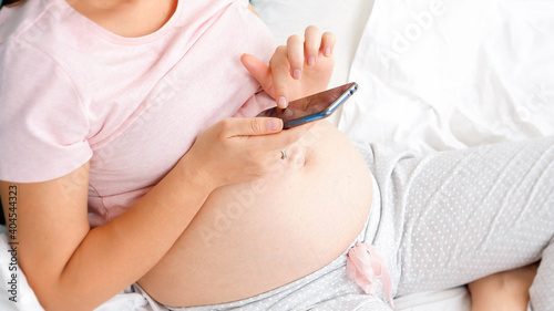 Top view shot of young pregnant woman with big belly browsing internet and using smartphone