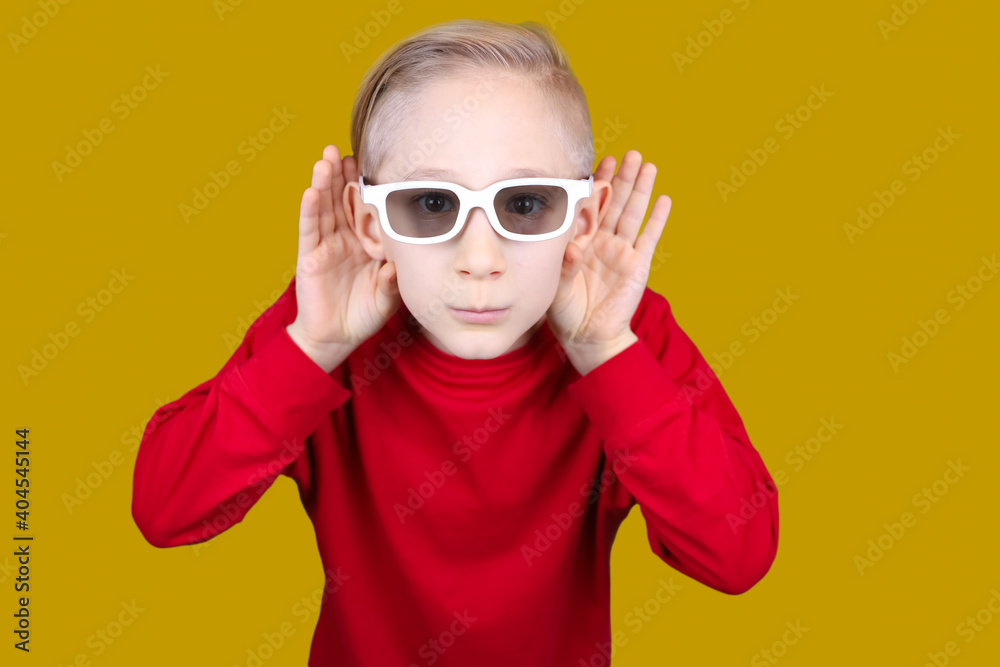 a child in 3D glasses puts his hand to his ear and tries to hear something a child in 3D glasses puts his hand to his ear and tries to hear something