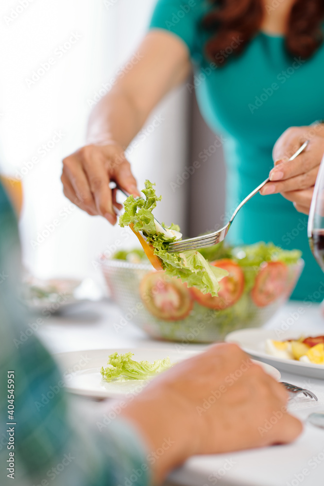 Housewife using tongs and fork when serving healthy vegetable salad for her guests at home