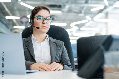 A happy female support operator is sitting at a desk and answering calls. Beautiful smiling woman talking to customers on a headset. Office employee in headphones.