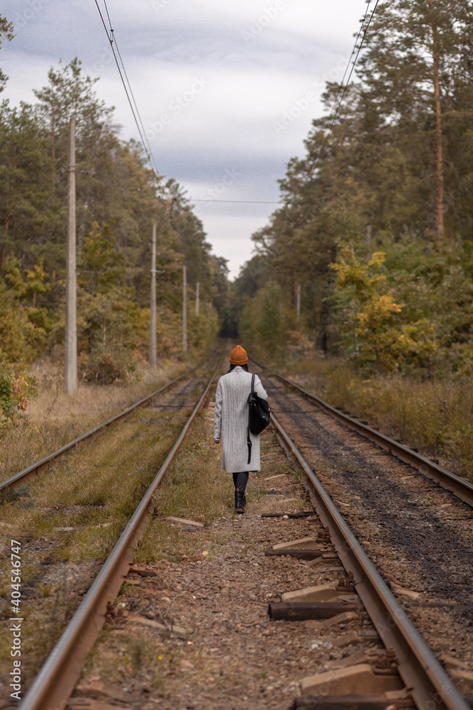 Fototapeta premium Girl tourist travels through the autumn forest along the railway.