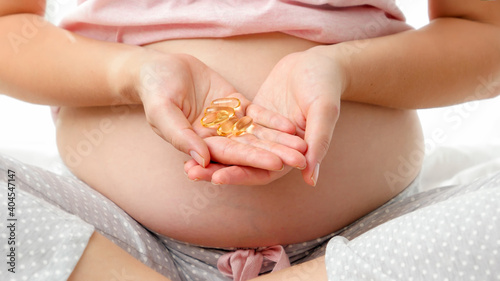 Closeup of young pregnant woman opens hands and holding pills with vitamins. Concept of pregnancy healthcare and female medical supplies