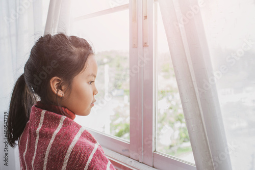 Sad little girl looks out the window. Stay at home awareness social media campaign and coronavirus prevention.