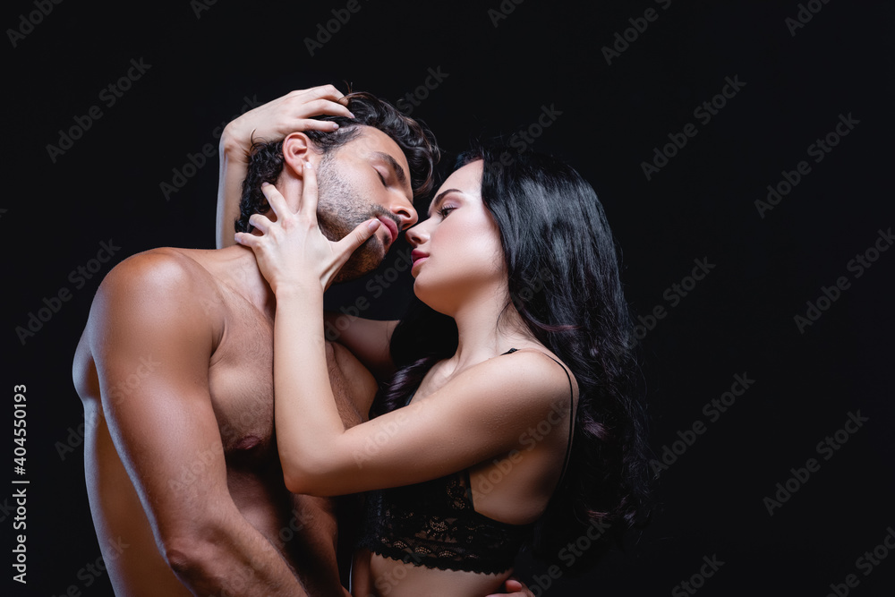 Φωτογραφία seductive brunette woman embracing head of young shirtless man isolated on black