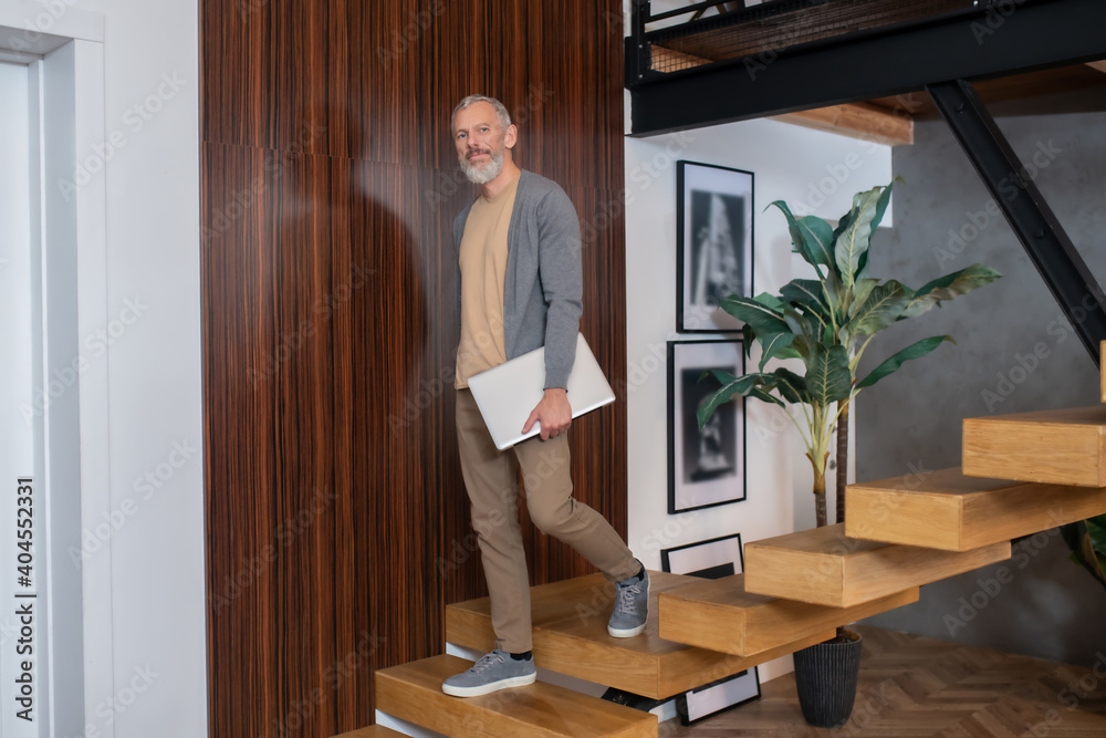 Grey-haired mature confident man holding laptop and going upstairs Grey-haired mature confident man holding laptop and going upstairs