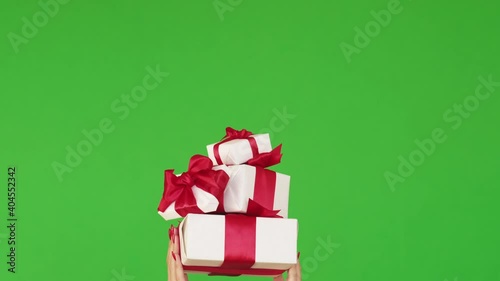 Women day sale. Holiday bonus. Special offer. Festive occasion present. Female hand showing pile of gift boxes with red ribbon bows isolated on green copy space background loop. photo