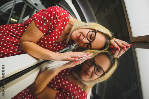 Mujer sonriente feliz rubia en un túnel estación de metro, con gafas y vestido rojo de manda corta con lunares blancos photo