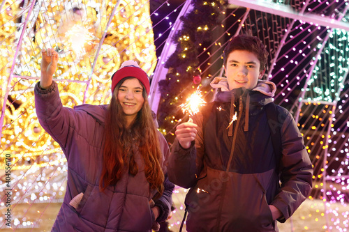 teenager boy and girl n street portrait with bengal fire sparkler on Christmas city illuminated decorations