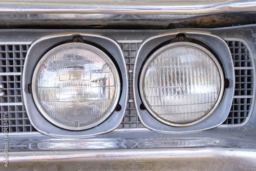 A headlight of a retro old car close up in a junk yard, changeover from old to a new modern car