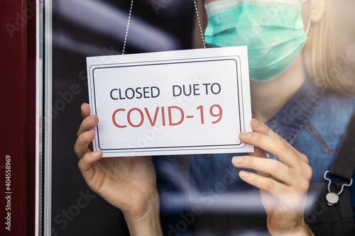 small business owner with face mask turning closed sign on shop window due to covid-19