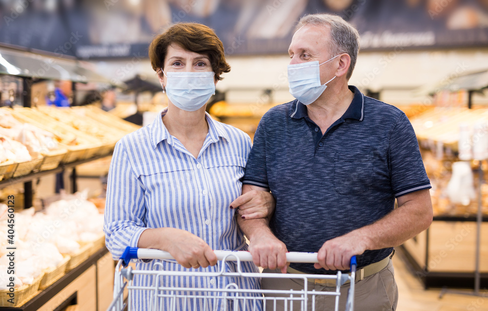 Man and woman in protective masks with shopping cart in supermarket