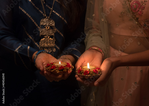Two pairs of hands holding Deepawali Diya or illuminated stylish and decorative lamps during a prayer ceremony at the onset of Deepawali festival which marks the victory of good over evil.
