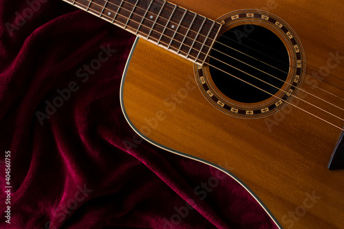 Top view acoustic guitar on burgundy red cloth fabric