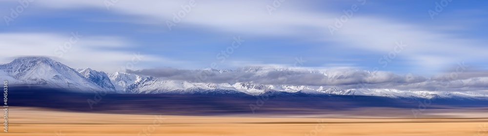 panoramic view of plain at root of snow-covered mountains on blue sky background