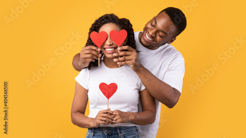 Black Husband Covering Wife's Eyes With Hearts Over Yellow Background photo