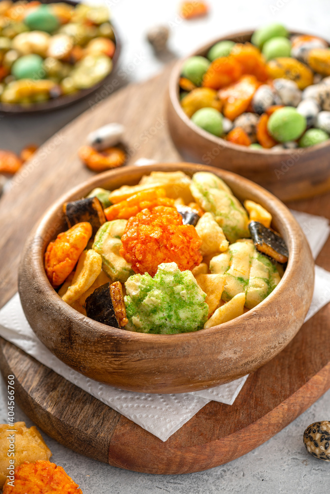 Various Japanese snacks in a wooden bowl close-up. Rice crackers with wasabi and nori, peanuts with sesame seeds, and other snacks. Mix traditional Japanese snack food. Various Japanese snacks in a wooden bowl close-up. Rice crackers with wasabi and nori, peanuts with sesame seeds, and other snacks. Mix traditional Japanese snack food.