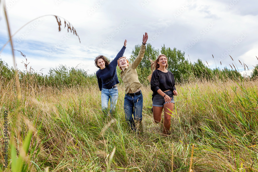 Summer holidays vacation happy people concept. Group of three friends boy and two girls running and having fun together outdoors. Picnic with friends on road trip in nature. Summer holidays vacation happy people concept. Group of three friends boy and two girls running and having fun together outdoors. Picnic with friends on road trip in nature.