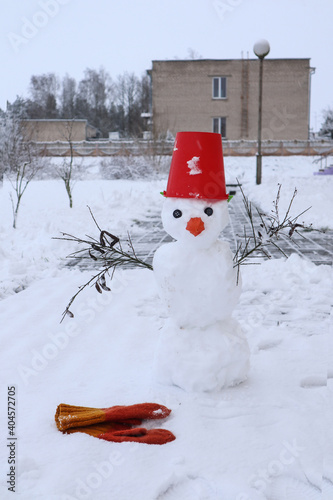 nowman with a red bucket instead of a hat on the background of buildings, yellow mittens, vertical frame - the concept of mobile winter games and entertainment photo