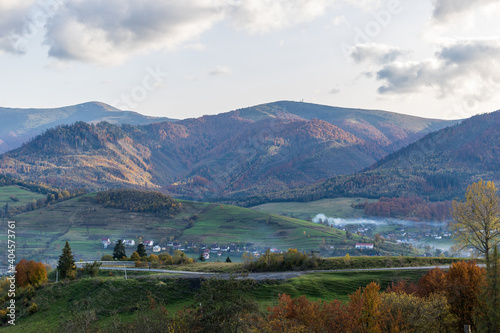 A small village located in a mountain valley. Autumn mountain landscape in the Ukrainian Carpathians - yellow and red trees combined with green needles. Panoramic view.