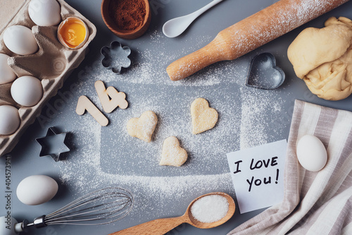 Making cookies for Valentine's Day, flat lay, top view, copy space. Various ingredients, rolling pin, dough, eggs, numbers 14, whisk on a gray background, layout on a gray background