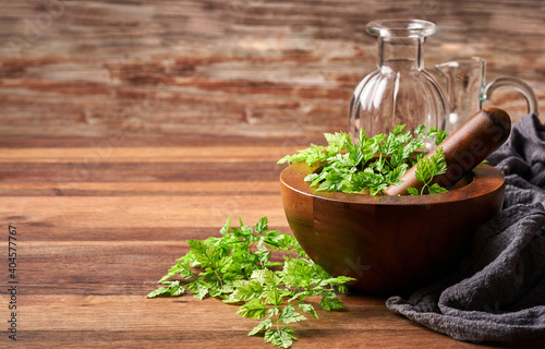 Photos concept of herb green chervil in a wooden mortar with glass bottles and fabric o