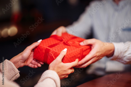 Valentine's Day concept. Close shot of man's and woman's hands presenting gifts to each other at a cafe. A young loving couple celebrating in the restaurant. New normal, winter holidays.