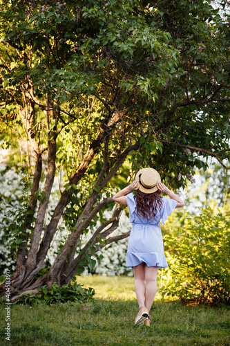 Summer mood. Romantic girl in Provence image and straw hat near beautiful tree. Spring or summer coming. Spring story. Brown-haired girl with long hairs. © Olga Mishyna