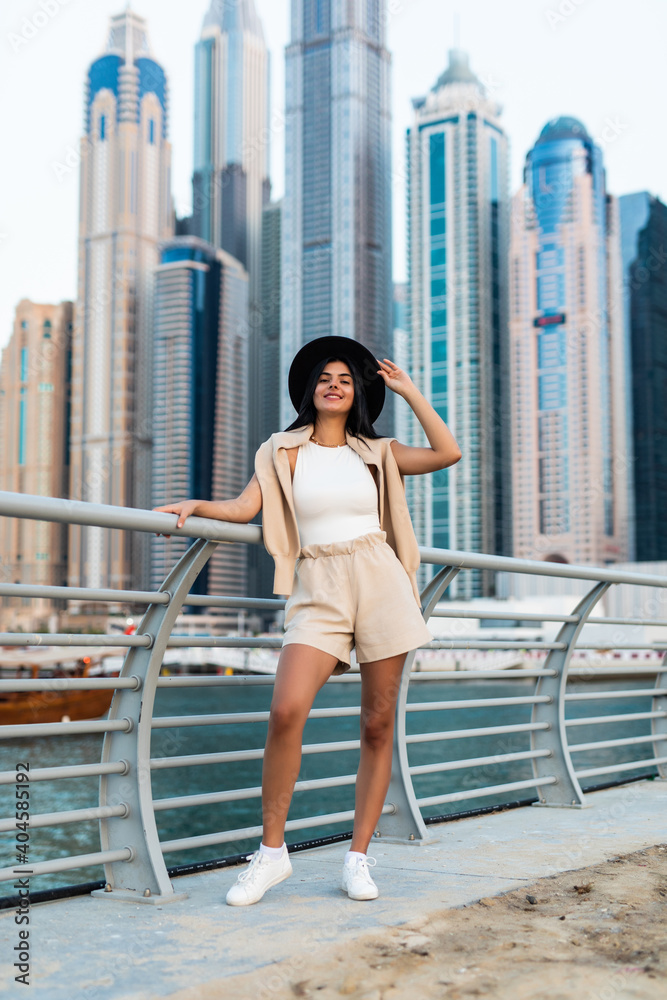 Young pretty woman in casual clothes walking on promenade in Dubai with skycrappers